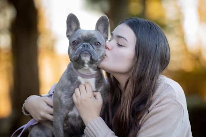 Woman kisses French Bulldog in autumn setting.