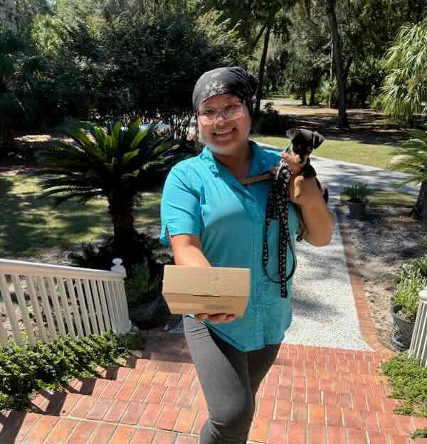 A delivery worker holds a package in one hand and her dog in the other hand while going up the stairs.
