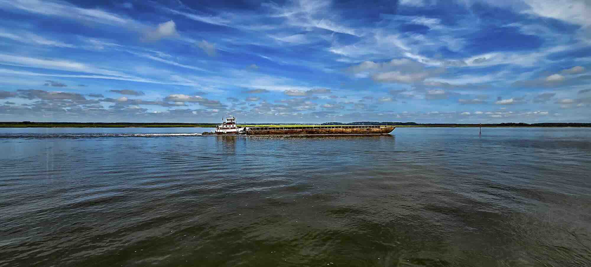 Tugboat navigating calm river under blue sky.