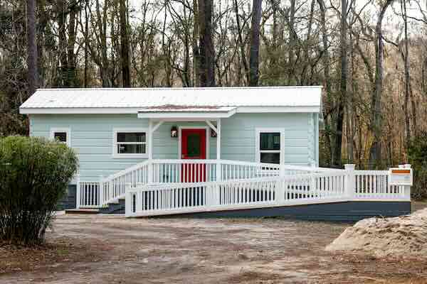 Accessible tiny house with ramp in wooded area.