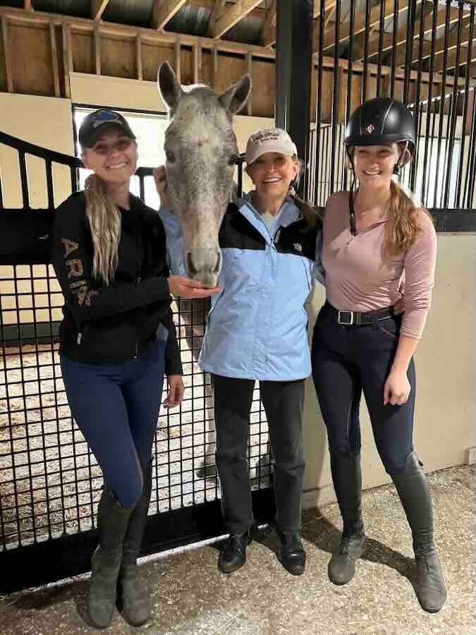 Three equestrians with a horse in a stable.