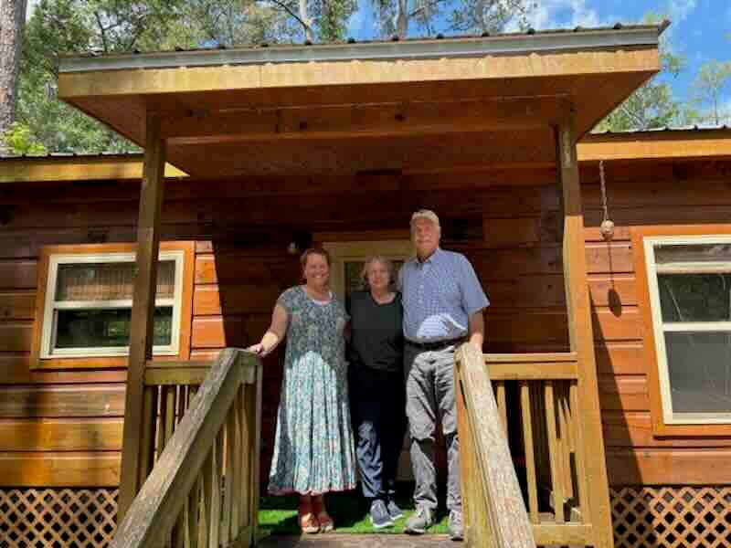 Three people standing on wooden porch of cabin.