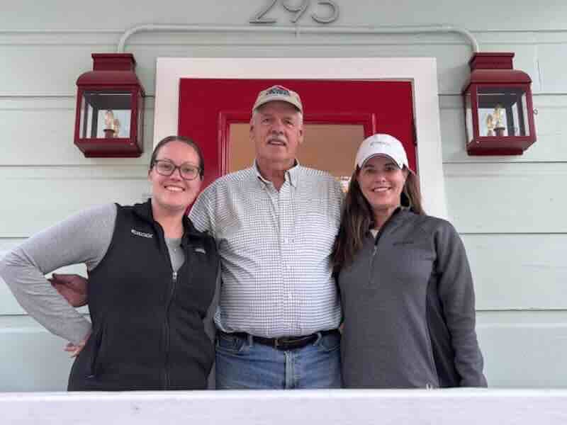 Three people smiling on a porch.